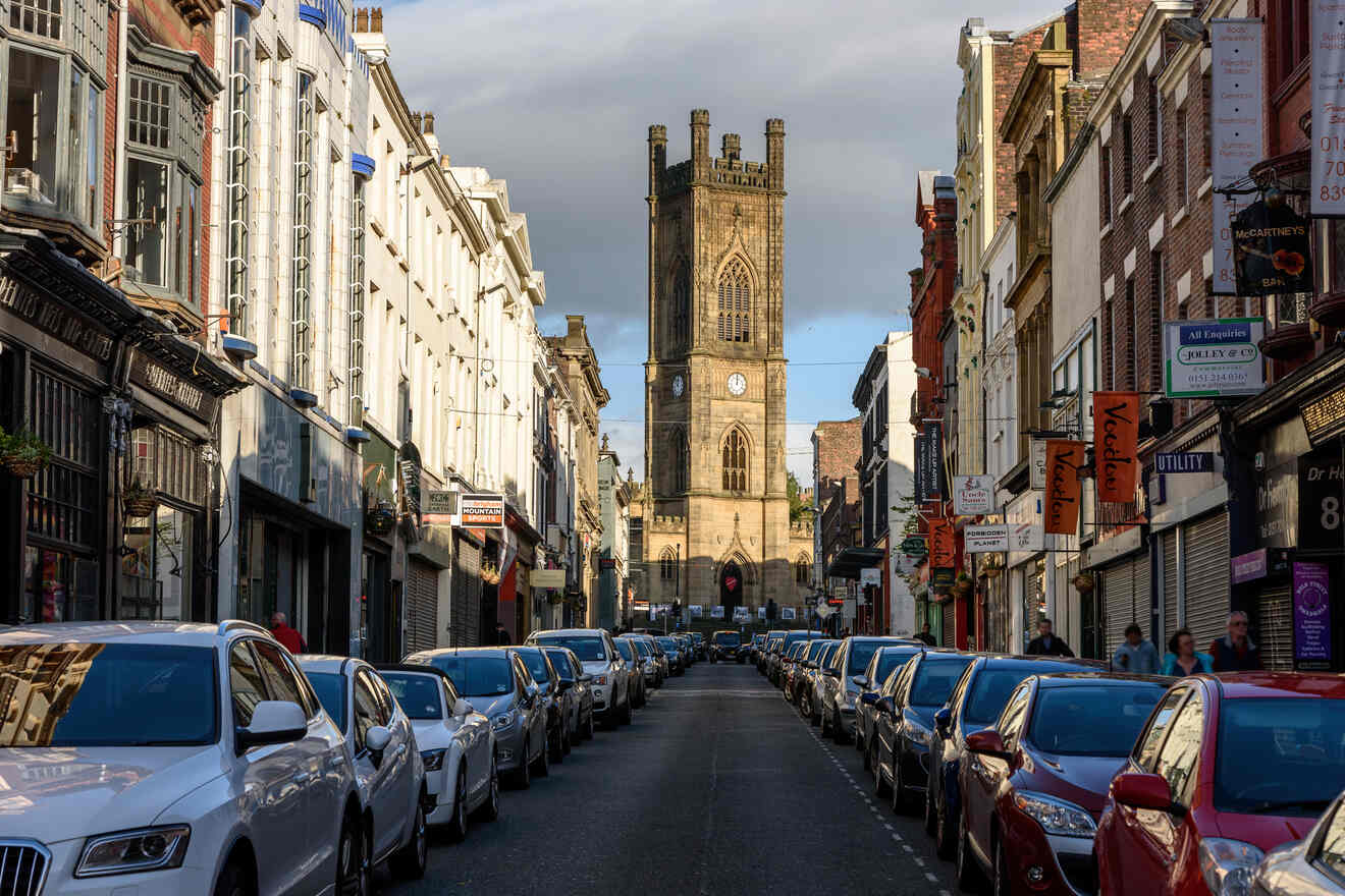 A historic street in Liverpool, lined with classic architecture leading towards the gothic tower of the Liverpool Parish Church under a blue sky